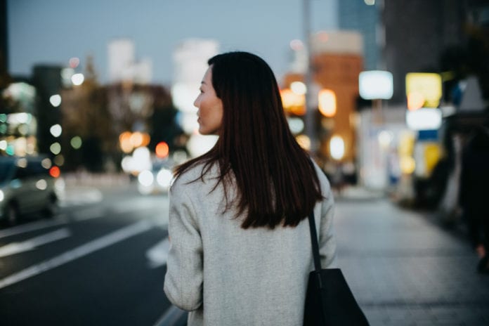 A woman faces away from the camera looking toward a city street