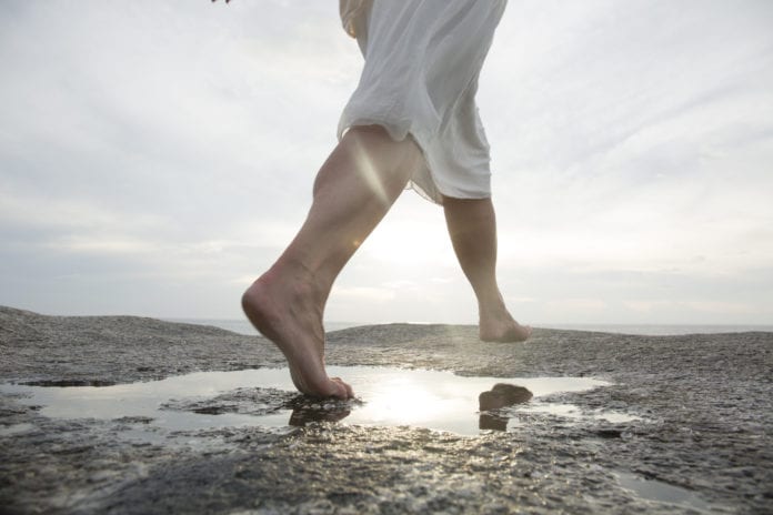 Woman leaps across rock slab pool, above sea