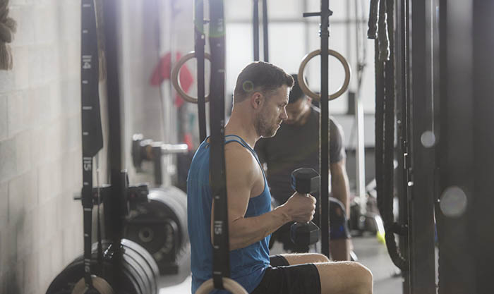 A man sitting on a bench in the gym lifting a hand weight