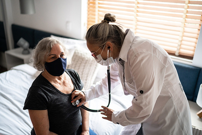 masked doctor listens to masked patient's heartbeat