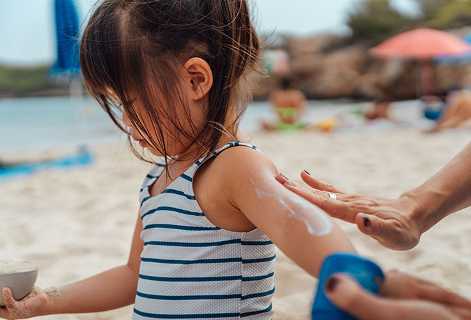 adult applying sunscreen to a child's arm while at the beach