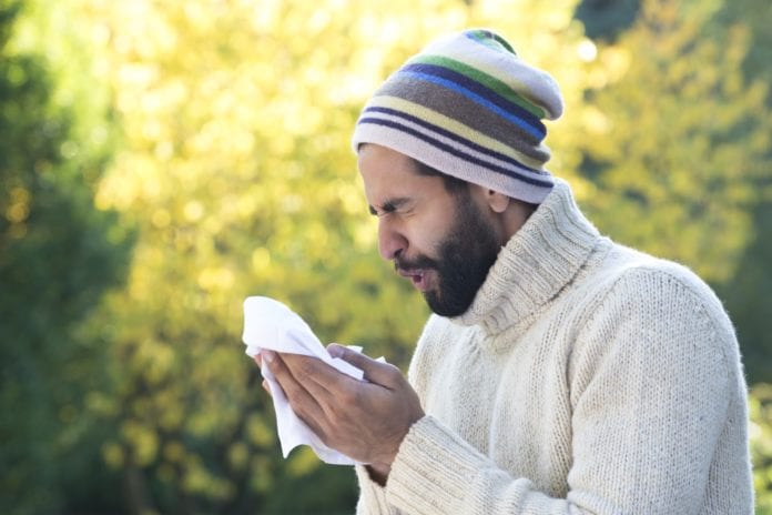 man wearing a sweater and hat sneezing