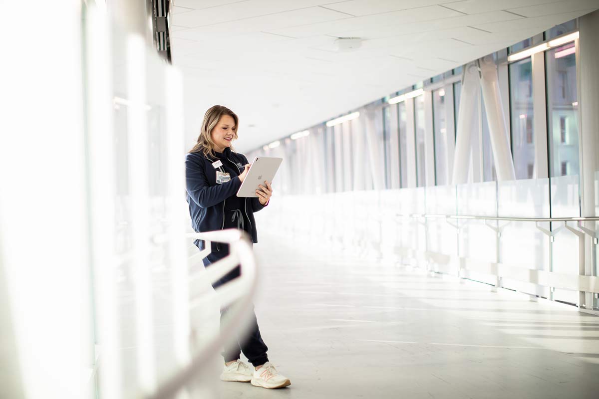 RN with clipboard and iPad in corridor.