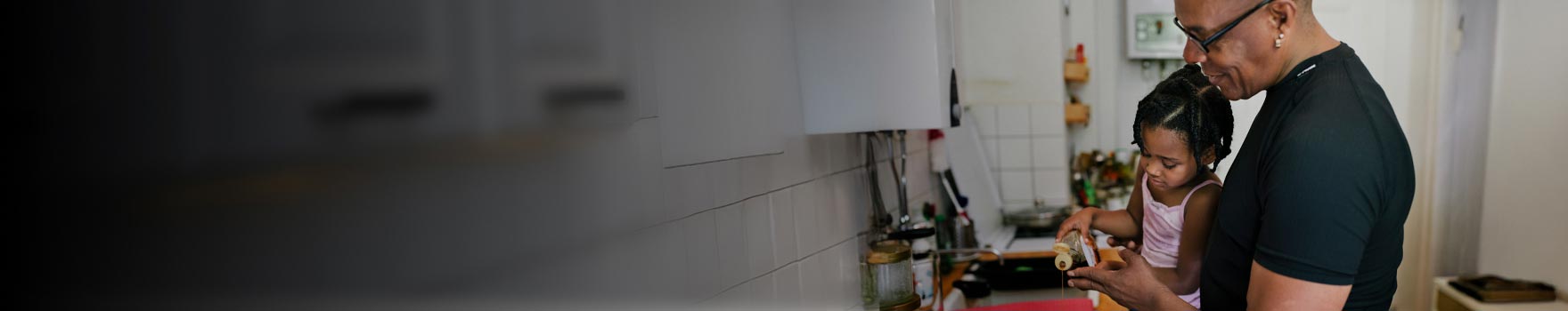grandfather wearing glasses helping young granddaughter in the kitchen