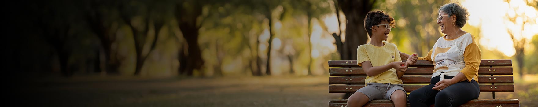 grandson chatting with grandmother on park bench, both wearing glasses