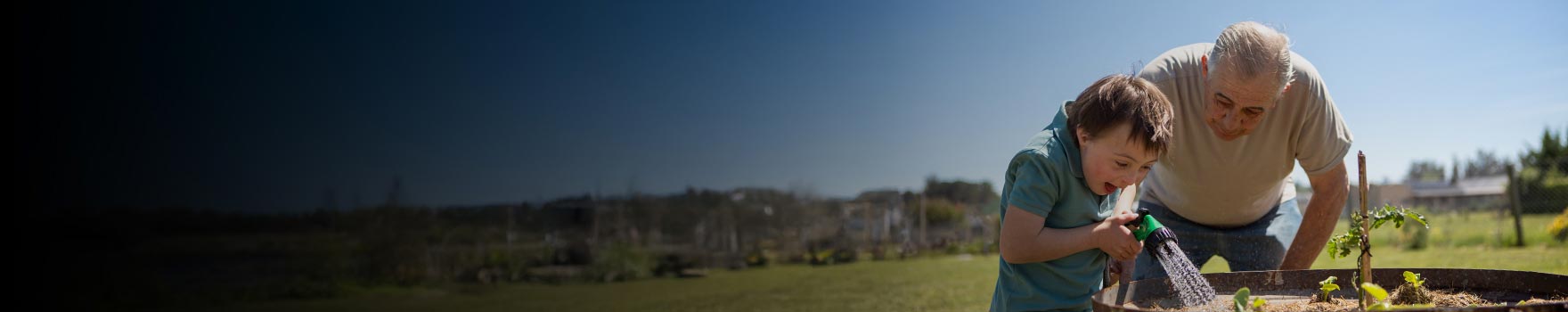 grandson watering plants with a hose, grandfather looks on