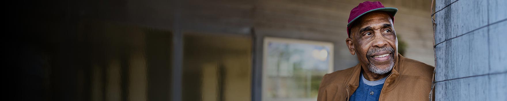 elderly man wearing a baseball cap leaning against a wall