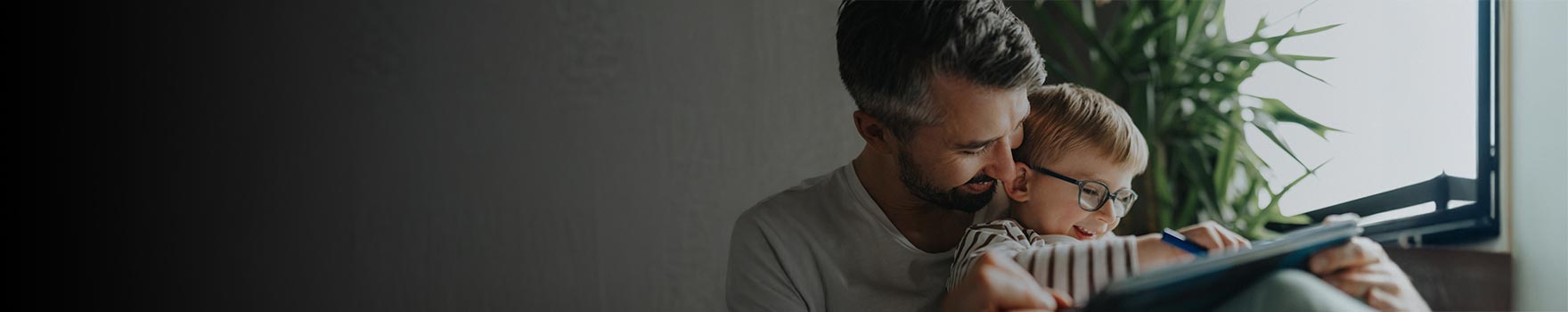 young boy wearing glasses and drawing while sitting in his father's lap