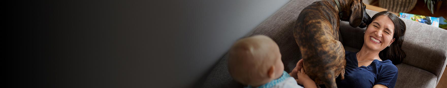 baby and dog atop woman lying down on sofa and laughing