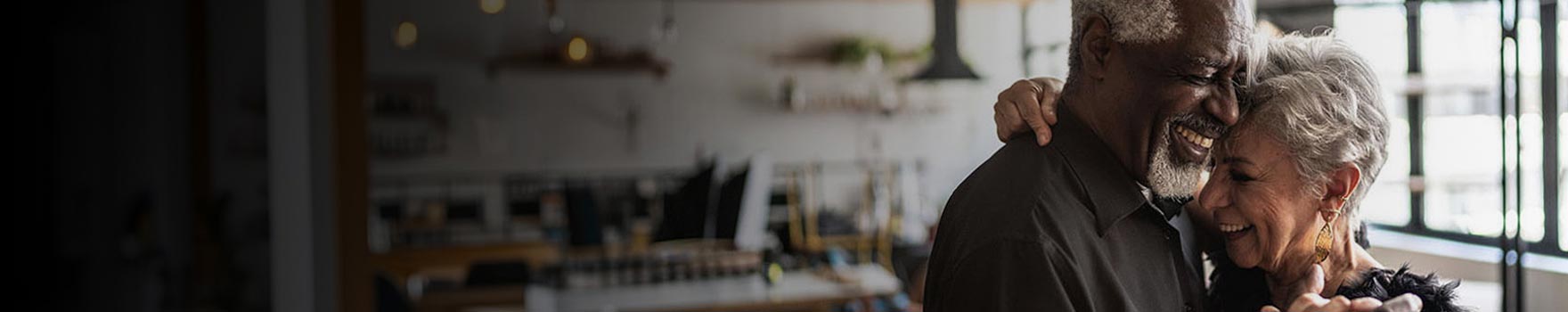 elderly man and woman hugging and laughing in their home