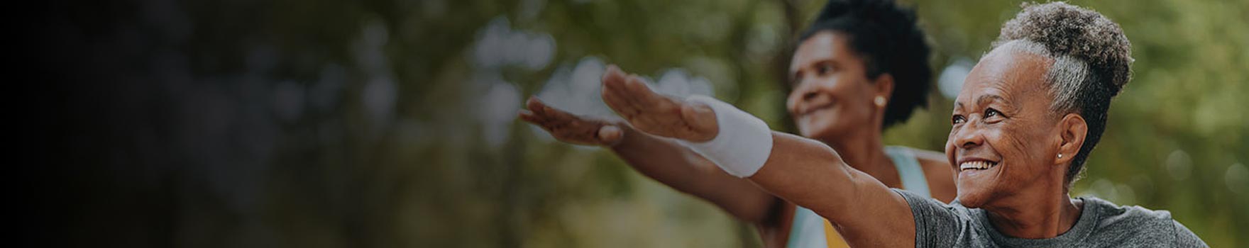 older woman practicing tai chi outdoors with another woman in same posture in the background