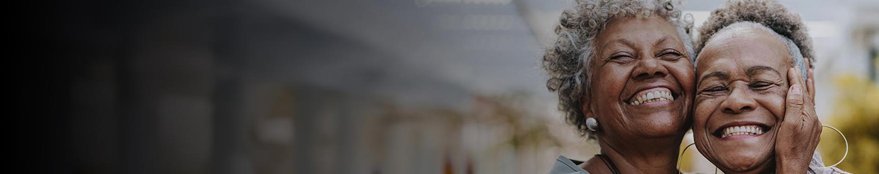 elderly woman holds another woman close as both of them smile