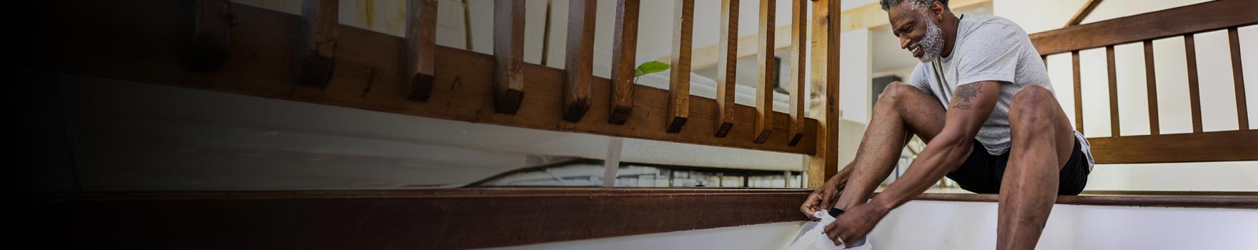 older man tying his shoe laces while sitting on the steps at his house