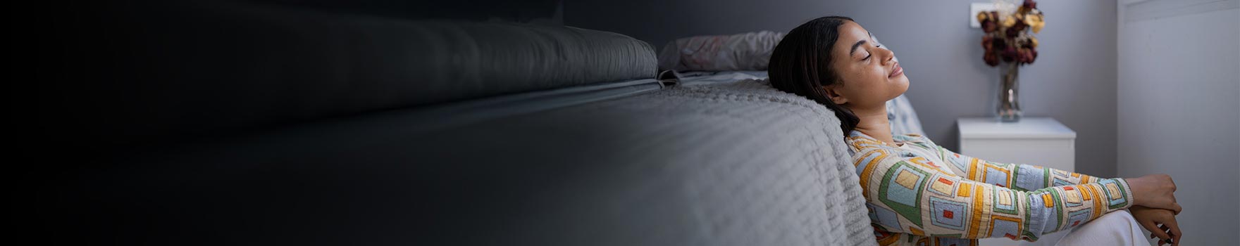 A young adult woman resting her head against the bed