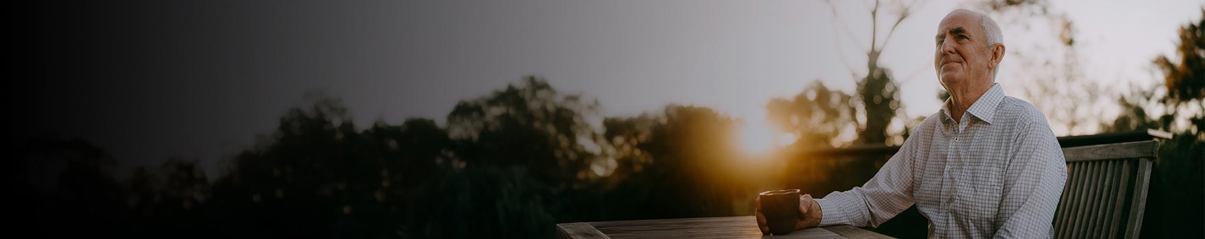 An older man sitting on a bench outdoors while drinking a warm beverage
