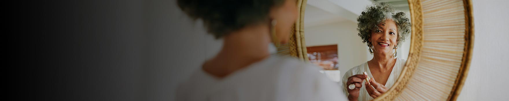 An older woman getting ready and looking at herself in the mirrow