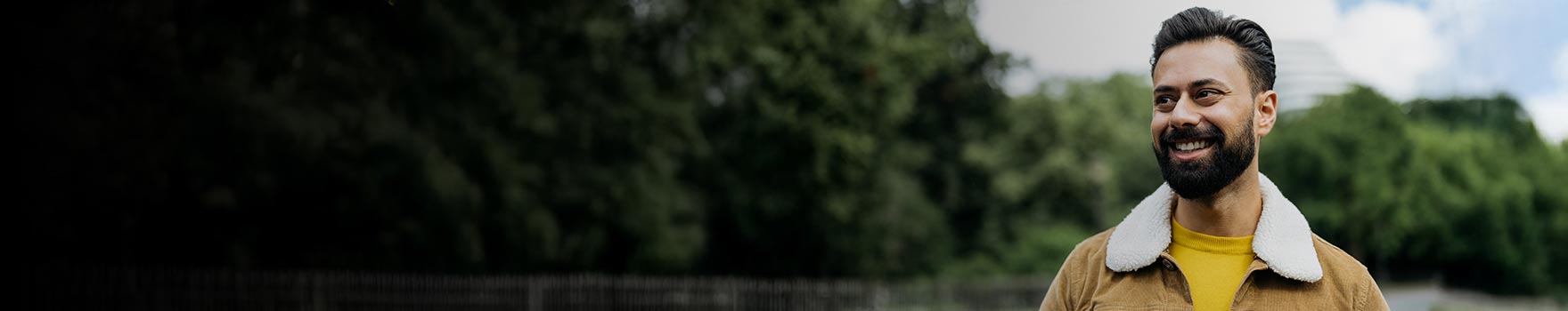 A man in his 30s smiling while walking on a park