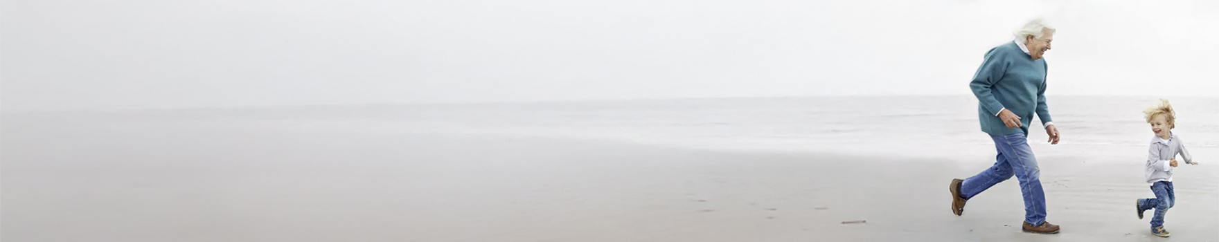 An elderly man running on the beach with their grandchild