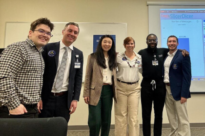 group with nametags poses in front of a presentation screen