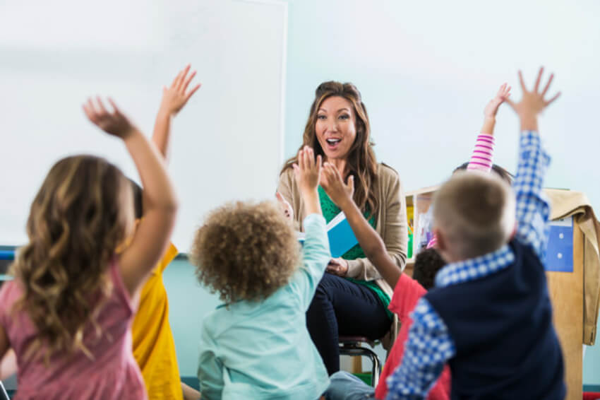 Children facing a teacher raise their hands