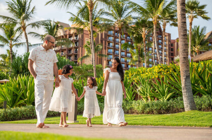 Divya and Ravi hold hands with their two daughters on a walk beneath the palm trees