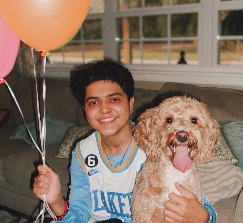 young man holding balloons next to dog