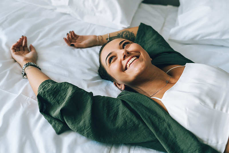 A cheerful woman relaxes on her bed, preparing to drift off to sleep.