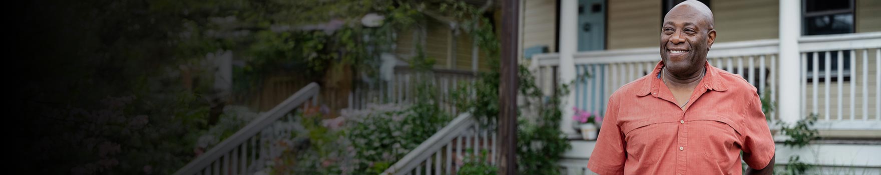 An older black man smiling outdoors in the front yard