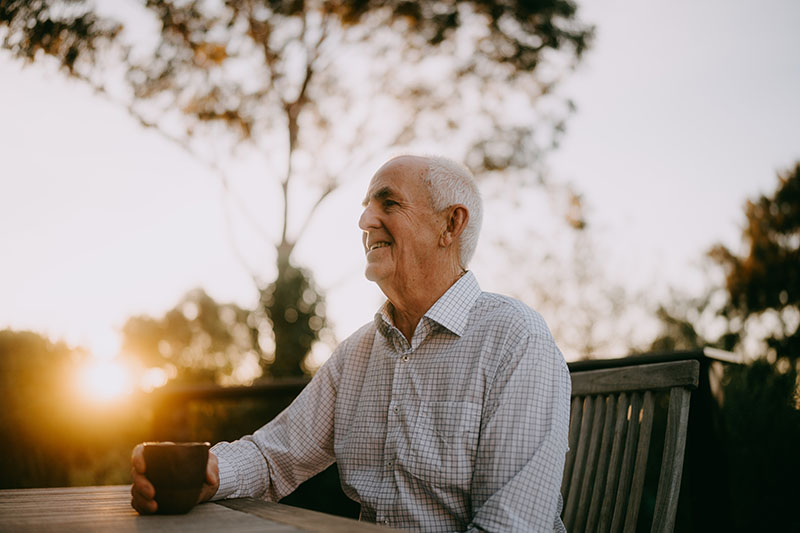 older man drinking coffee outdoors in the sunset