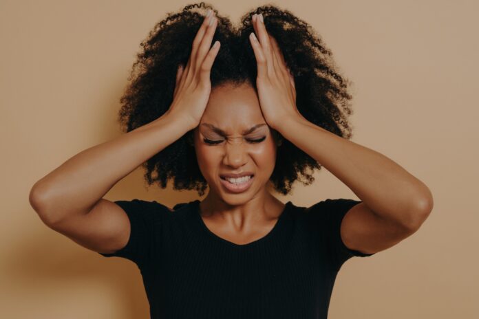 woman with headache pain with hands to temples while grimacing