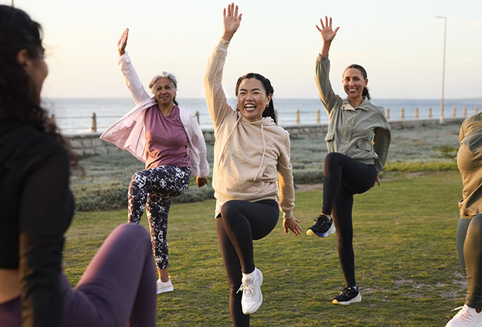Happy mature woman exercising in the garden with friends, following fitness instructor.